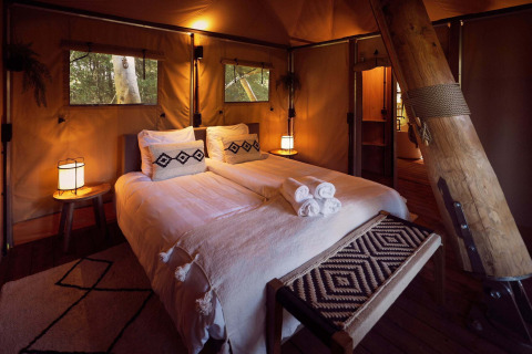 Innenraum eines Safari-Glampingzelts mit gemütlichem Doppelbett und warmem Licht im Resort de Parel, Niederlande.