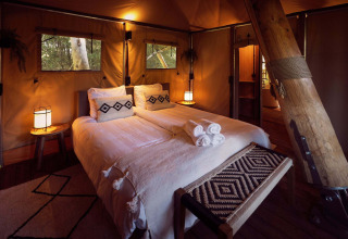 Innenraum eines Safari-Glampingzelts mit gemütlichem Doppelbett und warmem Licht im Resort de Parel, Niederlande.