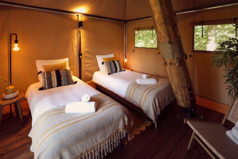 Interior de tienda glamping safari con dos camas, decoración acogedora y madera en Resort de Parel.