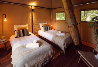 Interior view of a glamping safari tent with two cozy beds and wood accents at Resort de Parel.