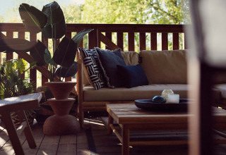 Gemütliche Terrasse im Glampingzelt Hacienda im Resort de Parel, Niederlande, mit Sofa und Pflanzen.