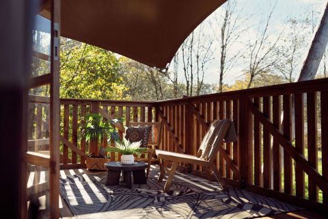 Terraza de madera soleada con sillas, plantas y toldo en Glamping tent Hacienda, Resort de Parel, Países Bajos.
