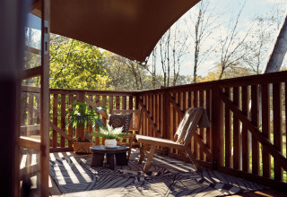 Solrigt trædæk med stole og planter under en baldakin ved Glamping tent Hacienda, Resort de Parel, Holland.