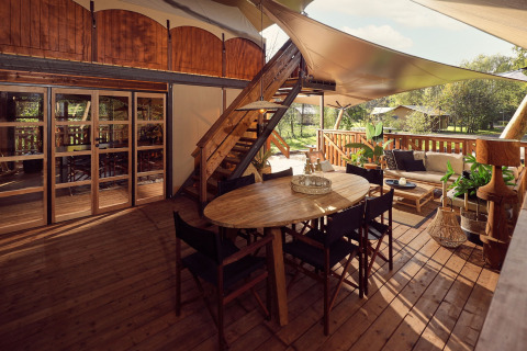 Tienda safari de glamping con terraza de madera, sala exterior y plantas en Resort de Parel, Países Bajos.