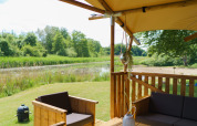Blick von einer Glamping-Zeltterrasse am See mit Holzmöbeln und grüner Natur im Resort de Parel, Niederlande.
