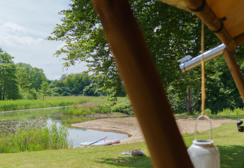 Vista da una tenda safari glamping su uno stagno e alberi presso Resort de Parel, Paesi Bassi, giornata di sole.