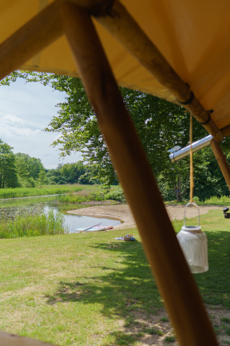 View from a glamping safari tent overlooking a pond and trees at Resort de Parel, Netherlands, sunny day.