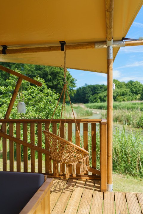 Hængestol på træterrasse under teltdug, glamping ved sø og skov på Resort de Parel, Holland.