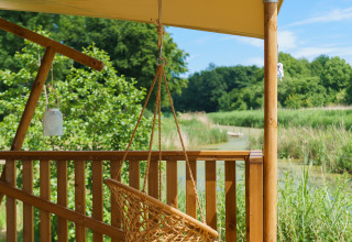 Hængestol på træterrasse under teltdug, glamping ved sø og skov på Resort de Parel, Holland.