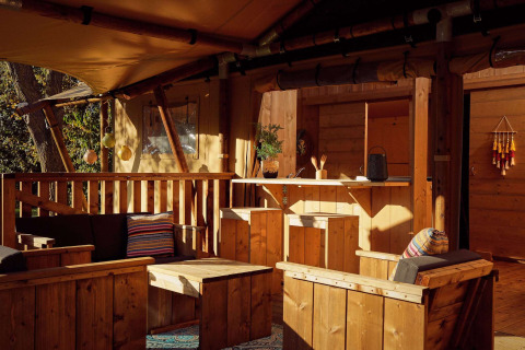 Terrasse de tente safari avec mobilier en bois, coussins colorés et ambiance chaleureuse en pleine nature.