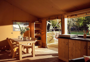 Interior photo of a safari tent kitchen and dining area with wooden furniture, terrace, and nature view.