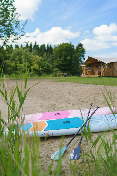 Safaritent La Vida Aqua met opblaasbare paddleboard en peddels op het zand bij Resort de Parel.
