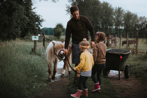 Una familia con dos niños y un adulto pasean un poni por un sendero verde en Feather Down Hoeve Brugge.