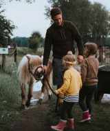 Una familia con dos niños y un adulto pasean un poni por un sendero verde en Feather Down Hoeve Brugge.