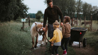 Una familia con dos niños y un adulto pasean un poni por un sendero verde en Feather Down Hoeve Brugge.