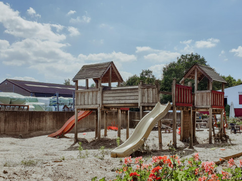 Speeltuin met houten constructies en glijbanen op een zonnige dag in Feather Down Hoeve Brugge, België.
