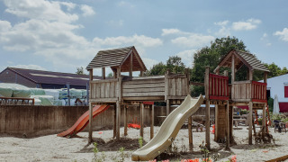Parque infantil con estructuras de madera y toboganes bajo el sol en Feather Down Hoeve Brugge, Bélgica.