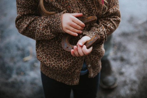 Un niño con chaqueta de estampado de leopardo sostiene una herradura oxidada en Feather Down Hoeve Brugge.