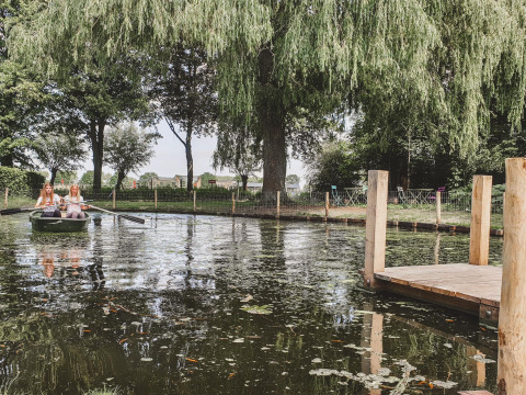 Twee vrouwen roeien in een boot op een vijver bij een houten steiger in Feather Down Hoeve Brugge, België.
