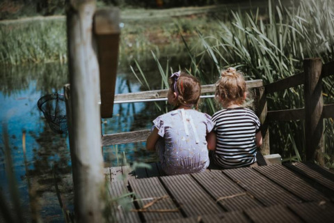 Twee jonge kinderen zitten op een houten steiger aan het water bij Feather Down Hoeve Brugge, België.