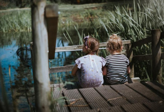 Twee kinderen zitten samen op een houten steiger aan het meer bij Feather Down Hoeve Brugge, België.
