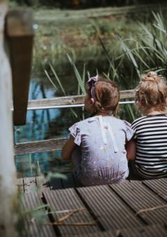 Dos niñas pequeñas sentadas en un muelle de madera junto al lago en Feather Down Hoeve Brugge, Bélgica.