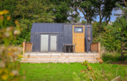 Pequeña casa moderna con terraza y sillas, rodeada de vegetación en Holiday Park Sallandshoeve, Países Bajos.