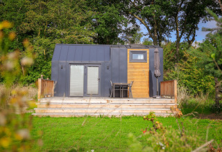 Tiny house moderna con terrazza in legno e sedie, immersa nel verde a Sallandshoeve nei Paesi Bassi.