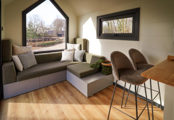 Intérieur d'une tiny house au Holiday Park Sallandshoeve avec canapé, tabourets de bar et grandes fenêtres.