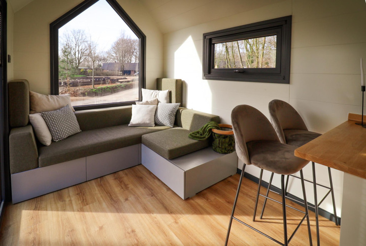 Innenraum eines Tiny House im Holiday Park Sallandshoeve mit Sitzbereich, Barhockern und großen Fenstern.