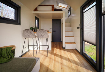 Interior de una tiny house moderna en Holiday Park Sallandshoeve, Países Bajos, con madera clara y grandes ventanas.