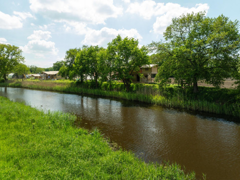 Vista de un río con césped, árboles y tiendas safari en Holiday Park Mölke, Países Bajos, durante un día soleado.