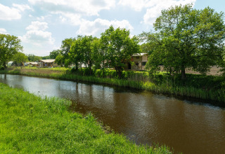 Vue sur une rivière bordée d’arbres et de tentes safari au Holiday Park Mölke, Pays-Bas, lors d’une journée ensoleillée.