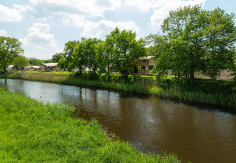 Vue sur une rivière bordée d’arbres et de tentes safari au Holiday Park Mölke, Pays-Bas, lors d’une journée ensoleillée.