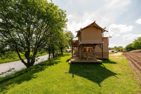 Safari-telt kaldet Treehouse tent ved floden på Holiday Park Mölke i Holland, omgivet af grønt.