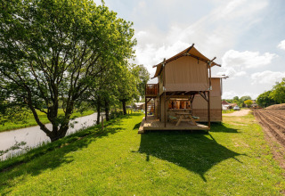 Safari-telt kaldet Treehouse tent ved floden på Holiday Park Mölke i Holland, omgivet af grønt.