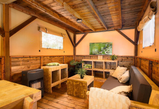 Gemütliches Wohnzimmer im Treehouse-Zelt mit Holzmöbeln und TV im Holiday Park Mölke, Niederlande.