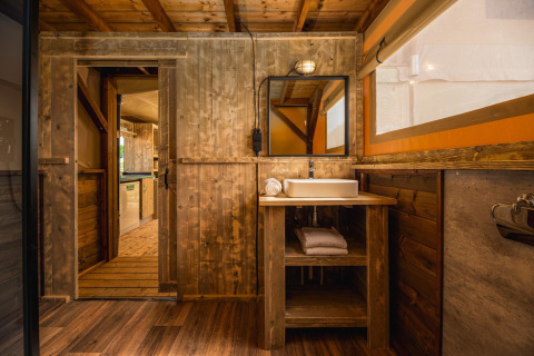 Rustikt badeværelse i safari-teltet Treehouse tent med vask, trævægge og håndklæder på Holiday Park Mölke.