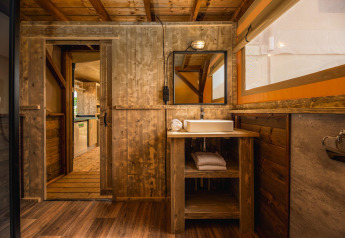Rustikt badeværelse i safari-teltet Treehouse tent med vask, trævægge og håndklæder på Holiday Park Mölke.
