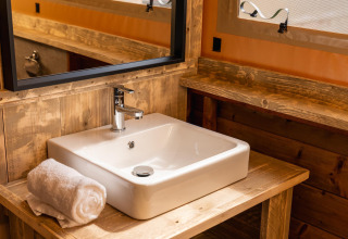 Lavabo y espejo con toalla enrollada en el interior de madera de la tienda Treehouse del Holiday Park Mölke, Países Bajos.