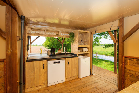 Keuken in een safaritent met uitzicht op groene velden en een beekje bij Holiday Park Mölke, Nederland.