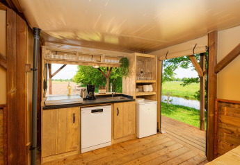 Area cucina in una tenda safari con vista su prati verdi e ruscello presso Holiday Park Mölke, Paesi Bassi.