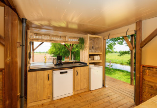 Kitchen area inside a safari tent overlooking green fields and stream at Holiday Park Mölke, Netherlands.