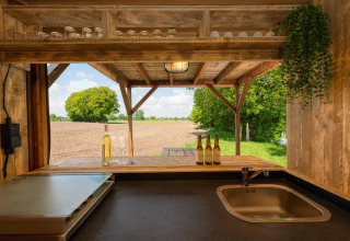 Udsigt fra et træhusteltkøkken med vask og bar ud over markerne på Holiday Park Mölke i Holland.
