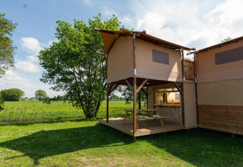 Safari-Baumhauszelt mit Terrasse und Picknicktisch im Holiday Park Mölke, Niederlande, mit Feldblick.