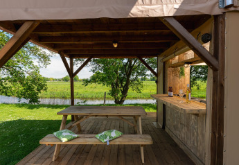 Overdekte zitruimte met houten tafel en bar aan safaritent in Holiday Park Mölke, Nederland.