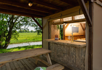 Gemütlicher Barbereich eines Safarizeltes mit Holztisch, Blick auf grüne Wiesen in den Niederlanden.