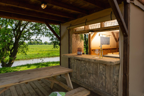 Charmante bar en picknicktafel in een safaritent met zicht op groene weilanden bij Mölke, Nederland.