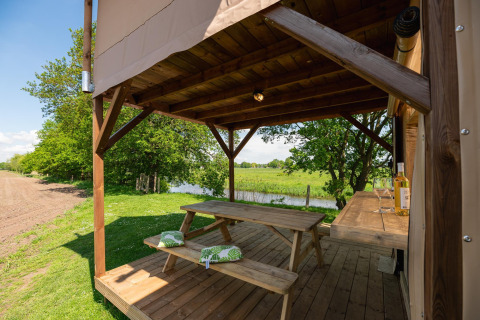 Træterrasse med picnicbord ved et safaritelts Treehouse på Holiday Park Mölke i Holland nær flod.