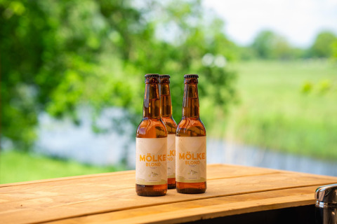 Drei Flaschen Mölke Blond Bier auf einem Holztisch mit grüner Natur im Hintergrund bei Holiday Park Mölke.